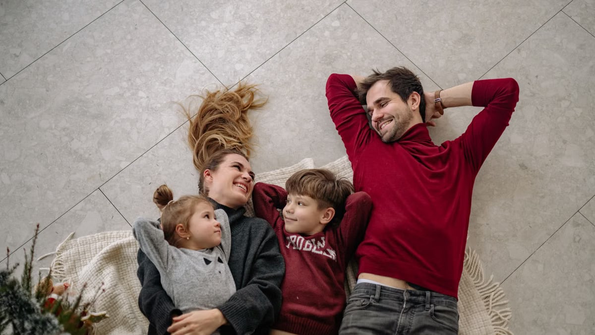 Smiling family of four lying on a blanket, sharing happiness and love indoors.